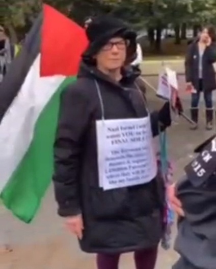 London 6.11.2023 - 1:44h: Eine
                j�dische Demonstrantin pr�sentierte die j�dischen
                Kriegsverbrechen auf einem A4-Blatt und trug eine
                Pal�stinenserfahne